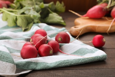 Photo of Towel with fresh ripe radishes on wooden table, closeup