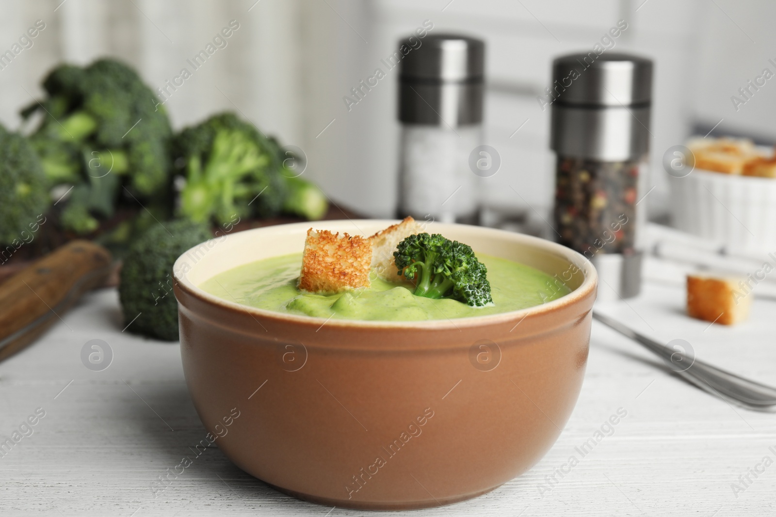 Photo of Delicious broccoli cream soup with croutons served on white wooden table