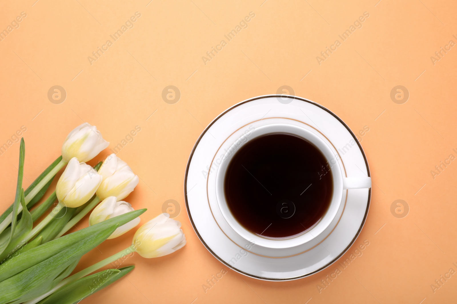 Photo of Cup of coffee and beautiful tulips on light orange background, flat lay