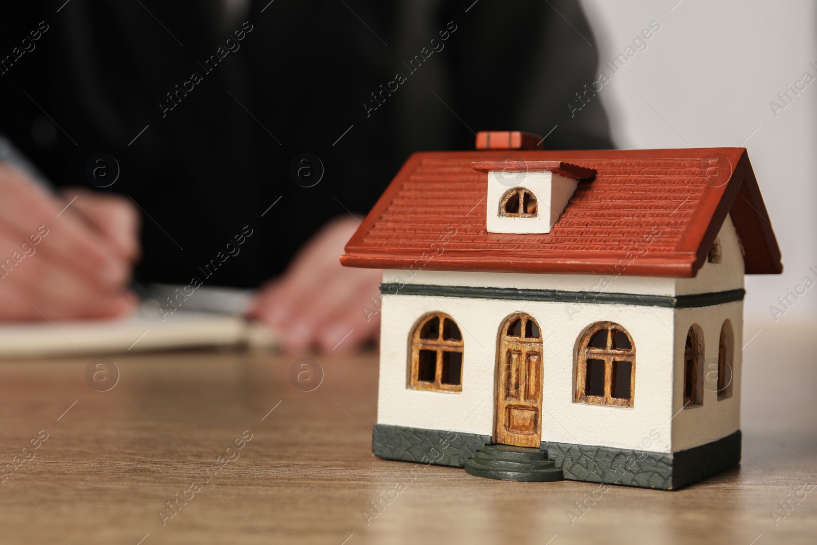 Photo of Mortgage concept. Woman writing at wooden table, focus on house model. Space for text