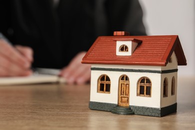 Photo of Mortgage concept. Woman writing at wooden table, focus on house model. Space for text