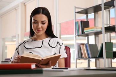 Young woman reading book at table in library