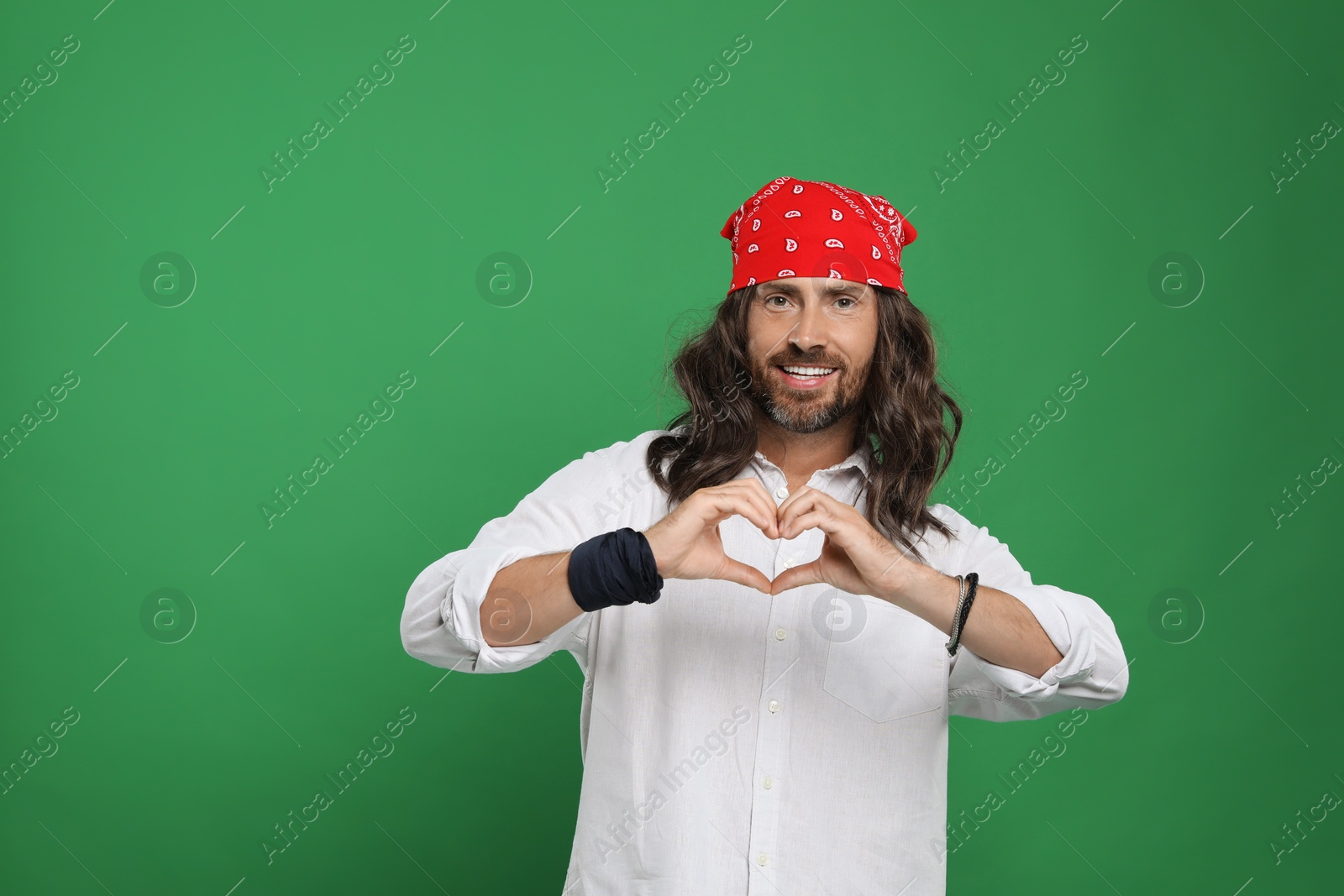 Photo of Hippie man making heart with hands on green background