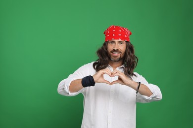 Photo of Hippie man making heart with hands on green background