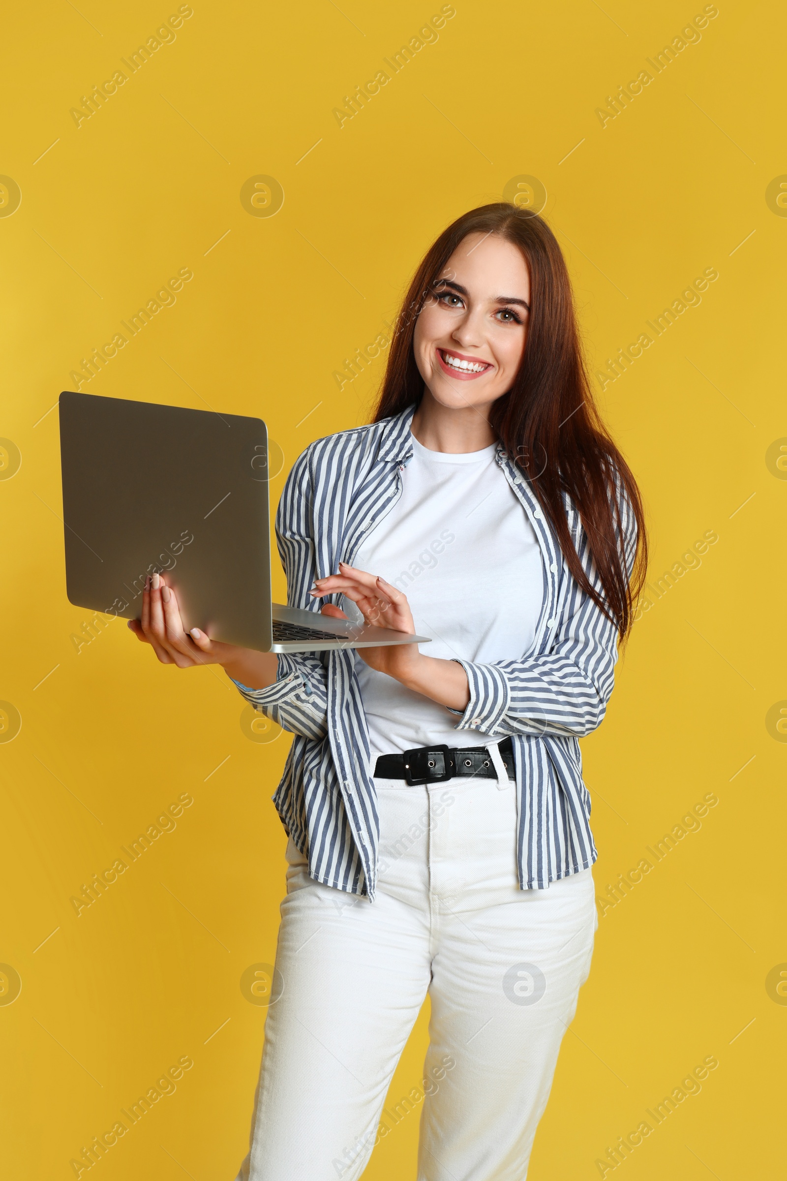 Photo of Happy woman with modern laptop on yellow background