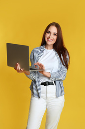 Photo of Happy woman with modern laptop on yellow background