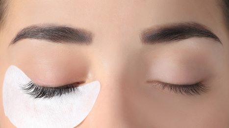 Young woman undergoing eyelashes extensions procedure, closeup