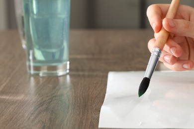 Photo of Woman painting with watercolor at wooden table, closeup. Space for text