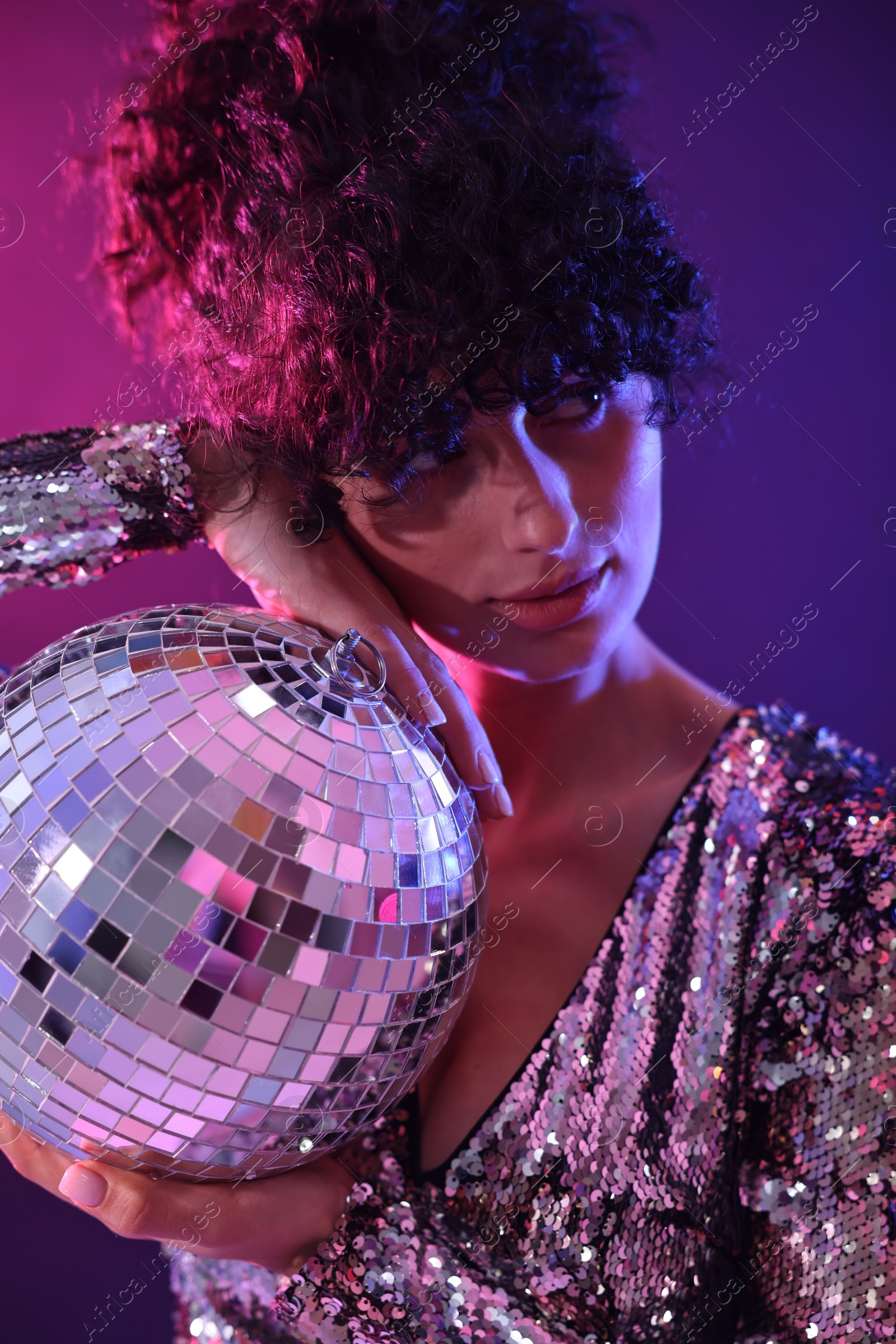 Photo of Beautiful young woman with disco ball posing on color background in neon lights