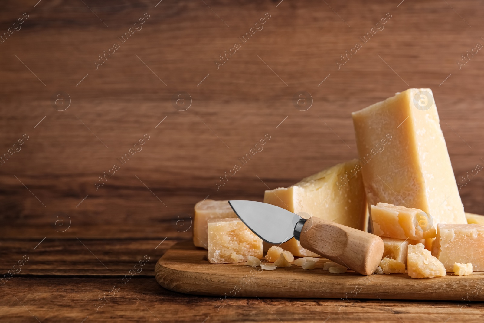 Photo of Pieces of delicious parmesan cheese with knife on wooden table. Space for text