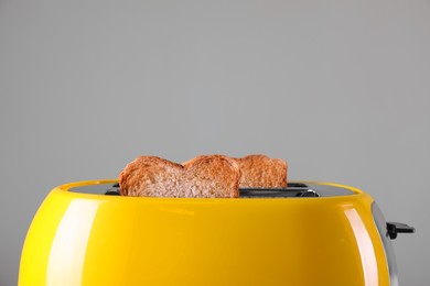 Modern toaster with slices of roasted bread against grey background, closeup. Space for text