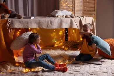 Kids having pillow fight in decorated play tent at home
