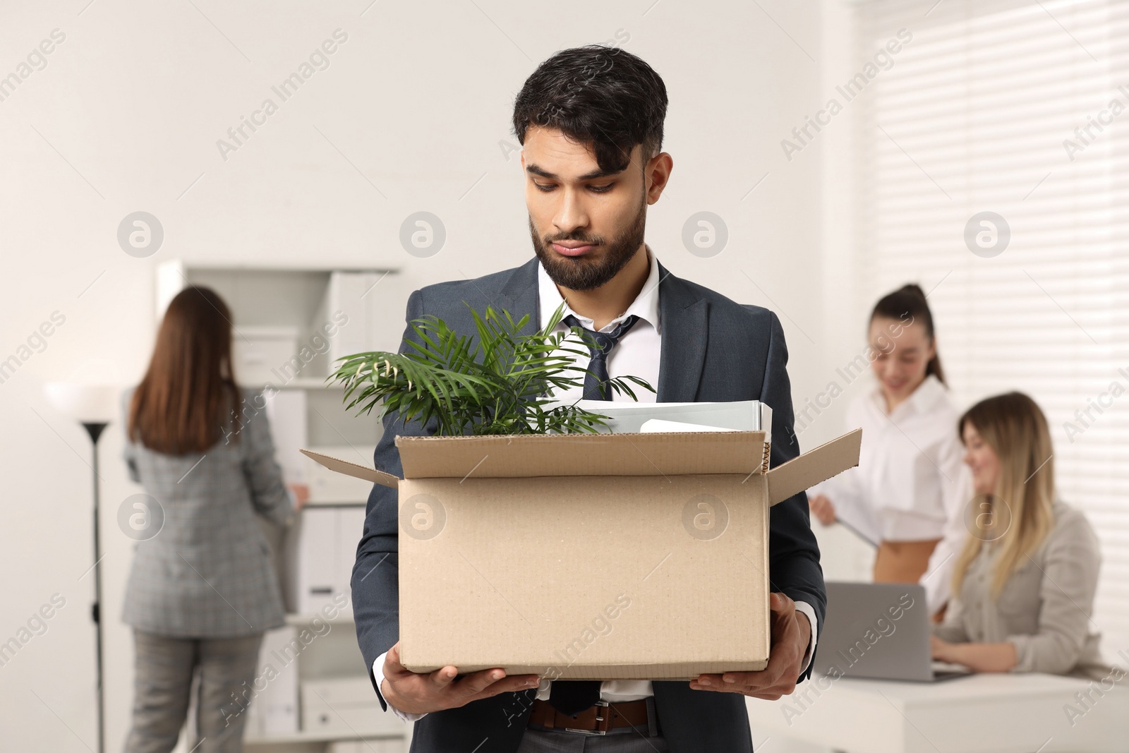 Photo of Unemployment problem. Frustrated man with box of personal belongings in office