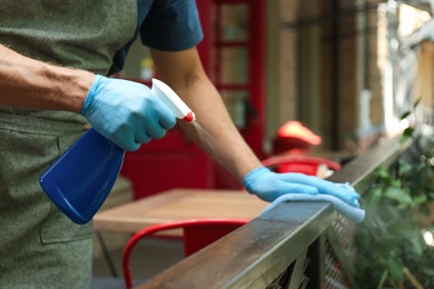 Photo of Worker in gloves disinfecting handrail outdoors, closeup