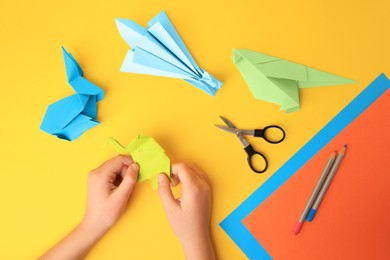 Photo of Origami art. Child holding paper figures on yellow background, closeup and top view
