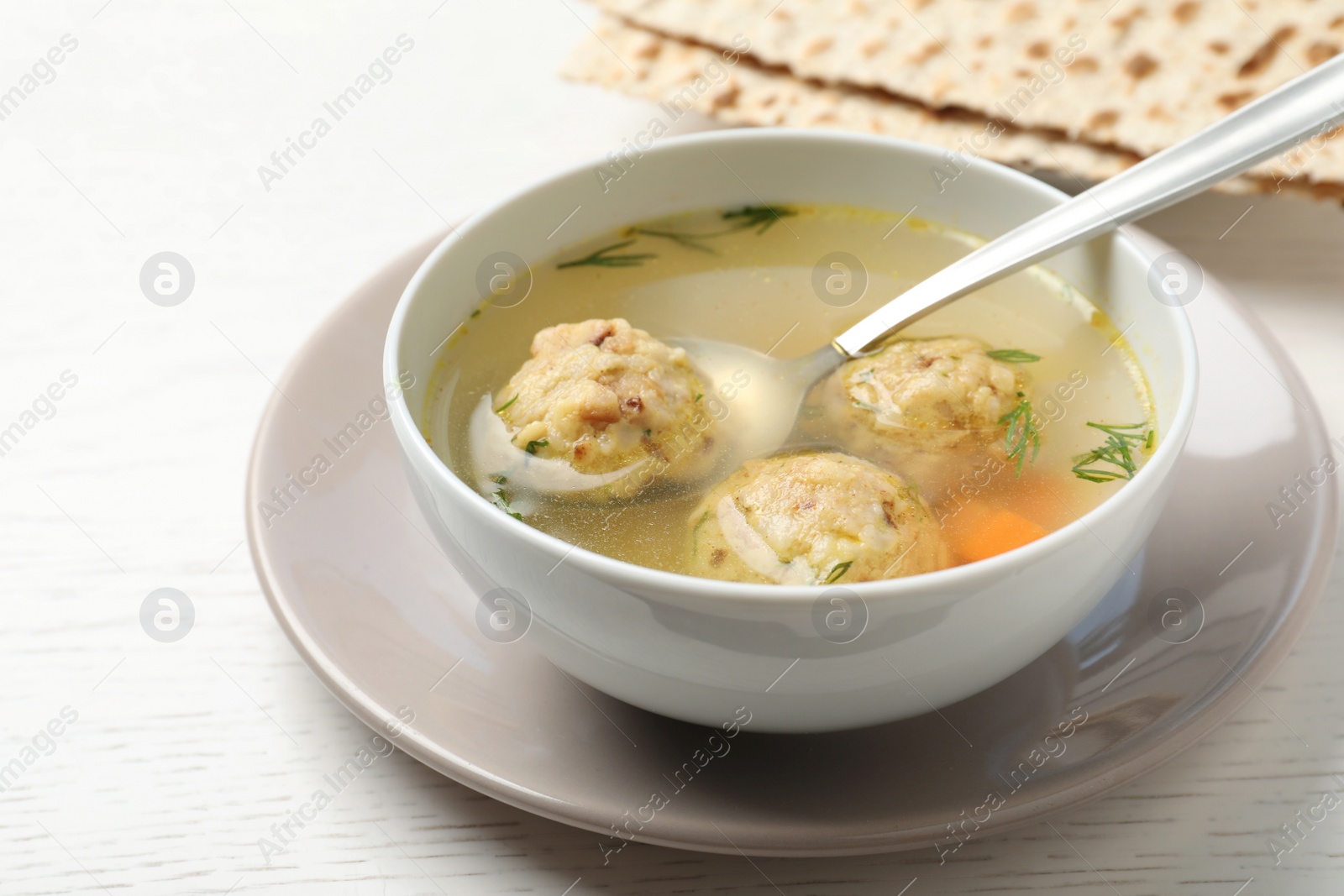 Photo of Bowl of Jewish matzoh balls soup on white wooden table