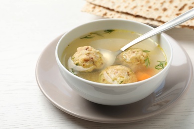 Bowl of Jewish matzoh balls soup on white wooden table