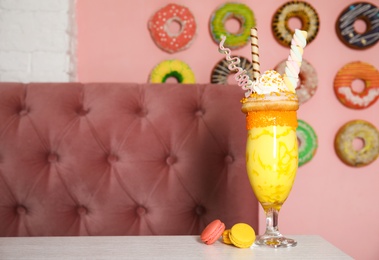 Glass of tasty milk shake with sweets on table indoors. Space for text