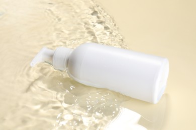 Photo of Bottle of face cleansing product in water against beige background