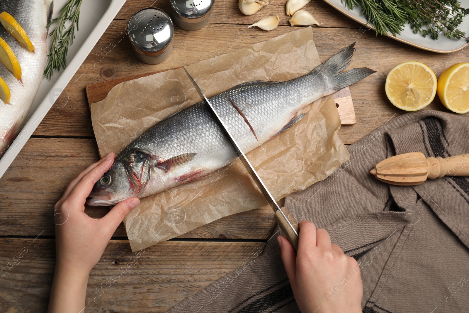 Photo of Woman cutting raw sea bass fish at wooden table, top view