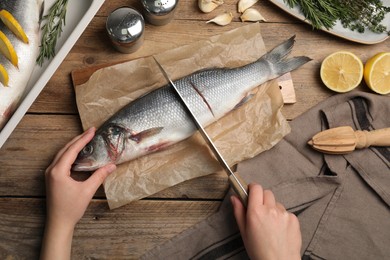 Photo of Woman cutting raw sea bass fish at wooden table, top view