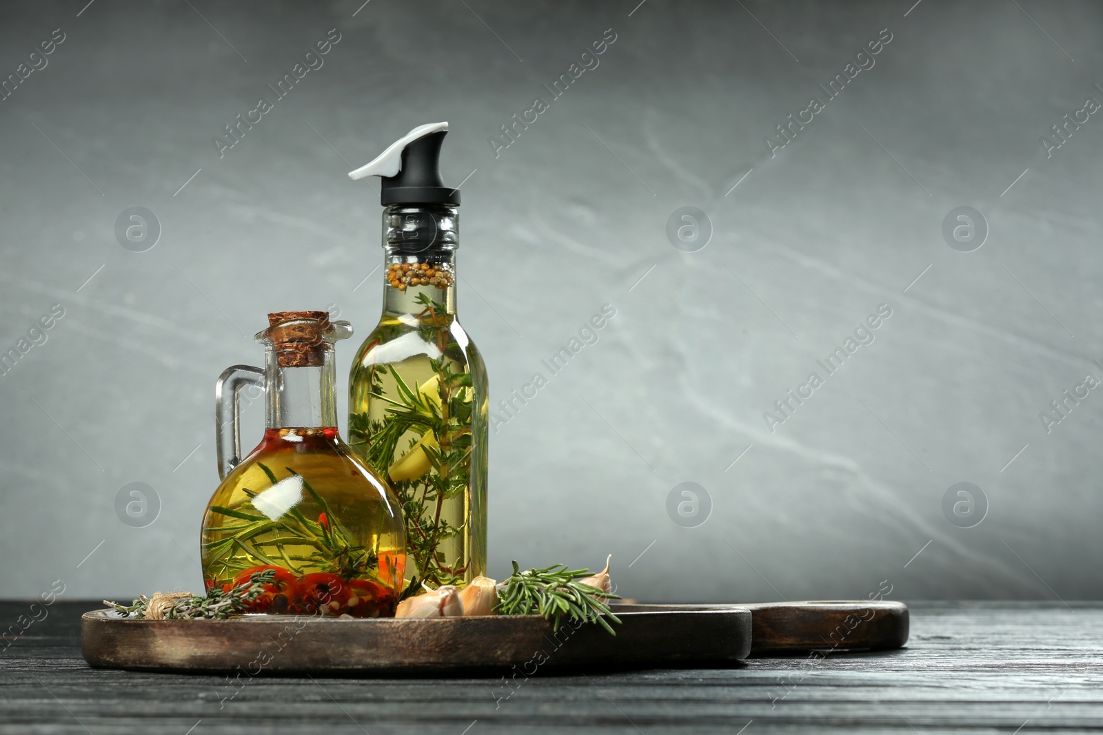 Photo of Cooking oil with different spices and herbs in bottles on dark wooden table. Space for text