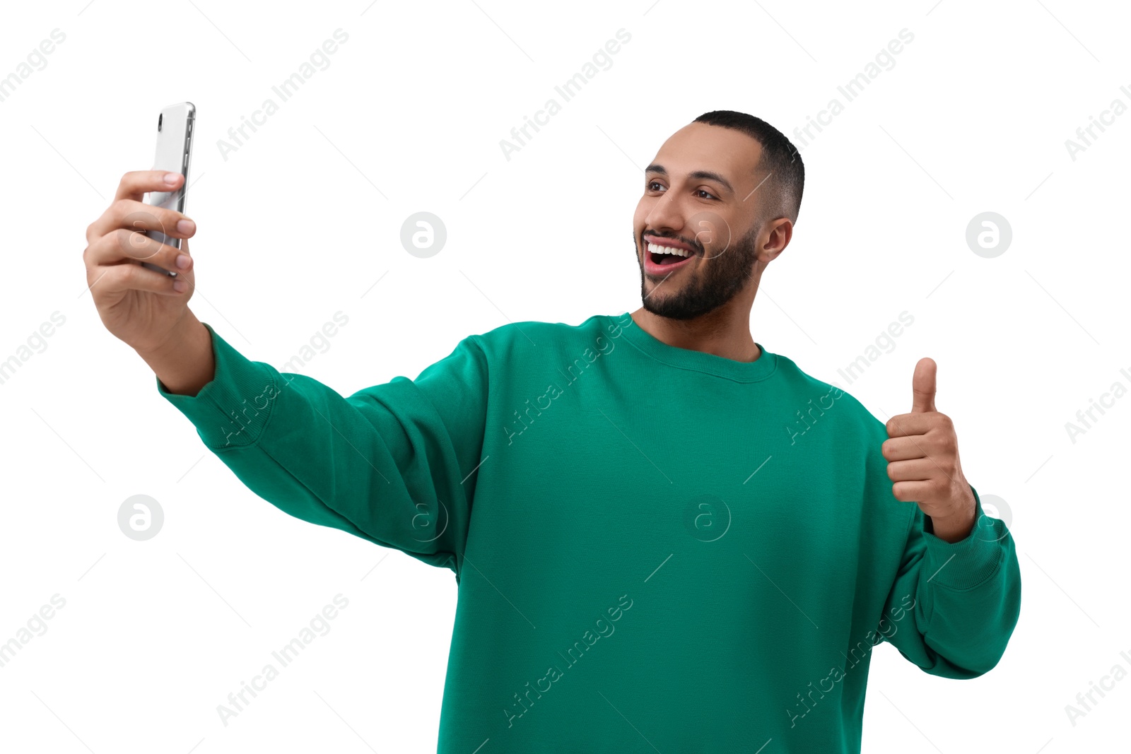 Photo of Smiling young man taking selfie with smartphone and showing thumbs up on white background