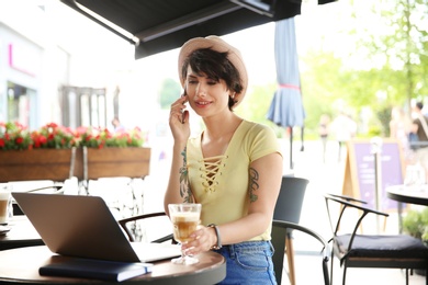 Young woman talking on phone while working with laptop at desk in cafe