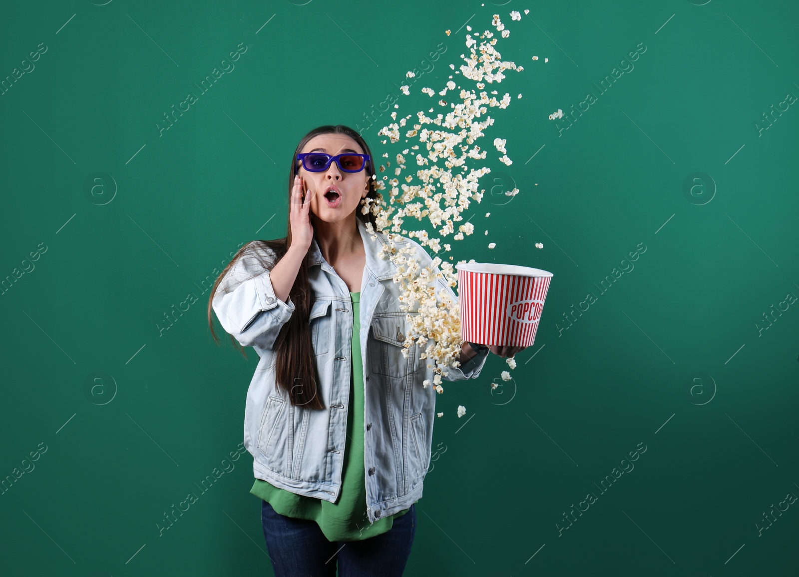 Photo of Emotional young woman with 3D glasses throwing popcorn on color background