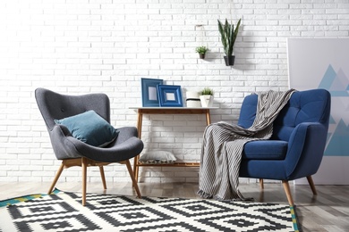 Photo of Modern interior with cozy armchairs and table near brick wall