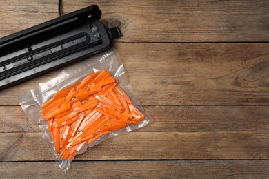 Photo of Vacuum packing sealer and plastic bag with cut carrots on wooden table, flat lay. Space for text