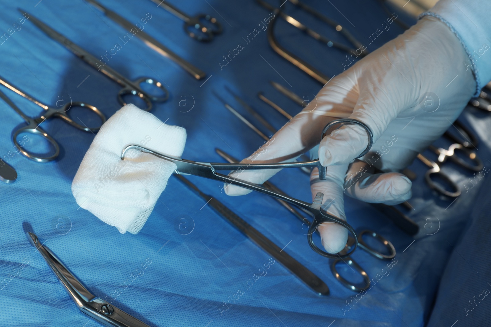 Photo of Doctor holding medical clamps with pad near table of different surgical instruments indoors, closeup