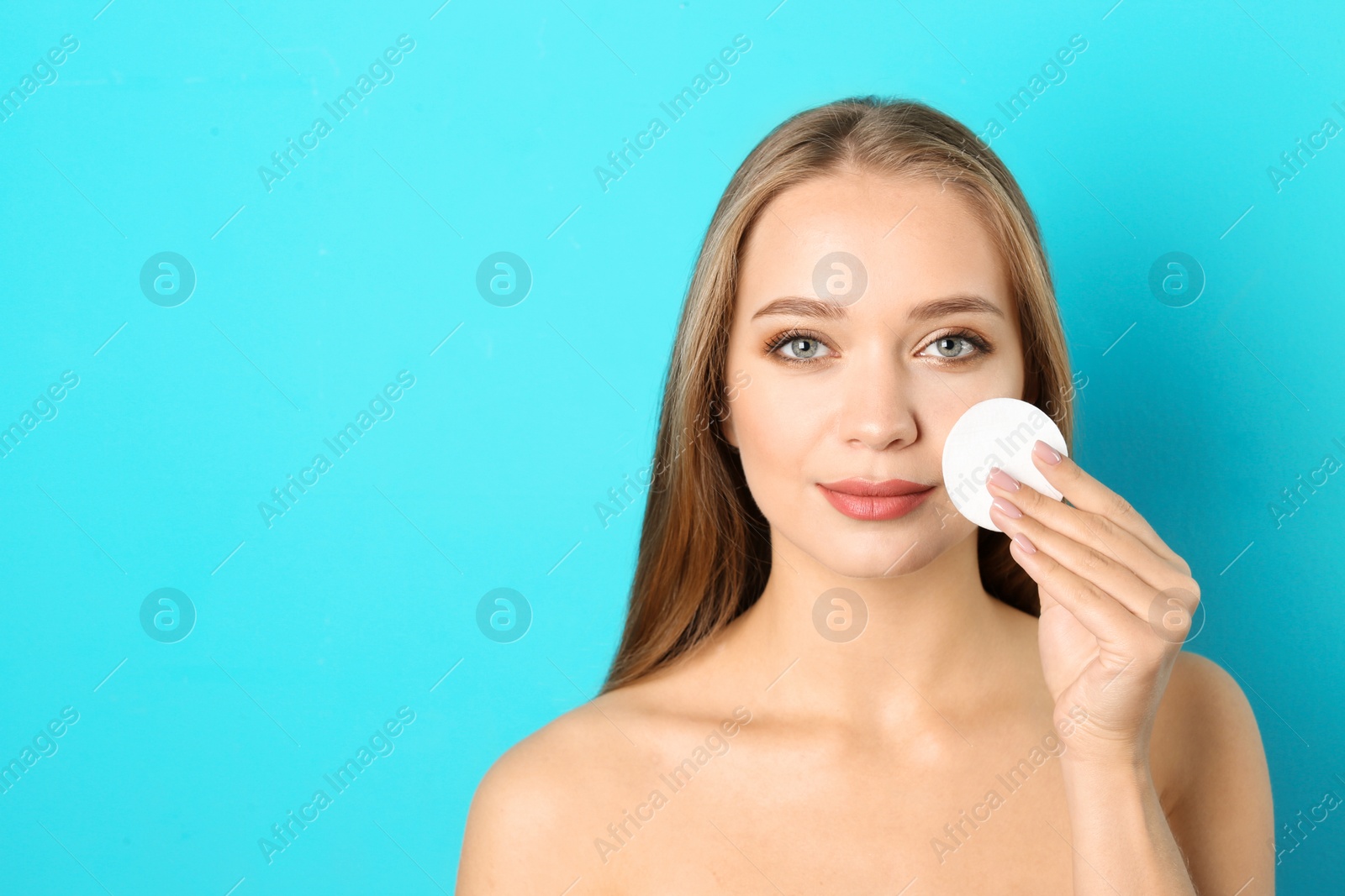 Photo of Portrait of beautiful young woman removing makeup with cotton pad on color background. Space for text