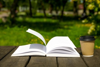 Photo of Open book and paper coffee cup on wooden table outdoors
