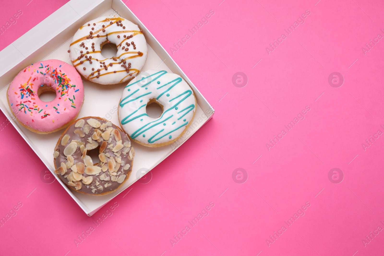 Photo of Box with different tasty glazed donuts on pink background, top view. Space for text
