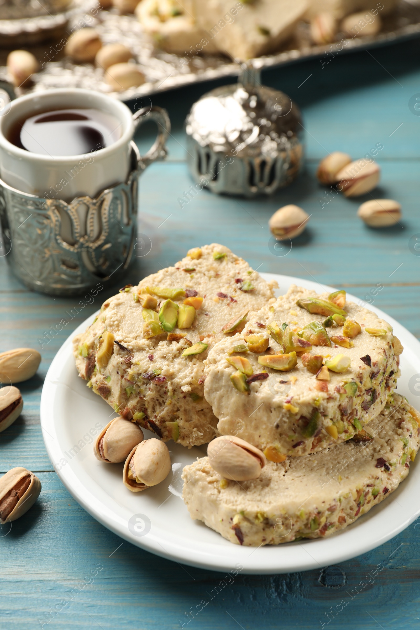 Photo of Tasty halva with pistachios served on light blue wooden table