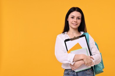 Photo of Smiling student with notebooks and clipboard on yellow background. Space for text