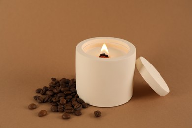 Photo of Burning soy candle and coffee beans on brown background