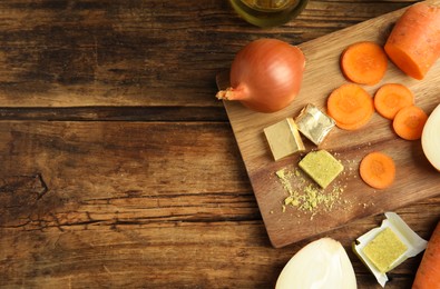 Photo of Bouillon cubes, carrot and onions on wooden table, flat lay. Space for text