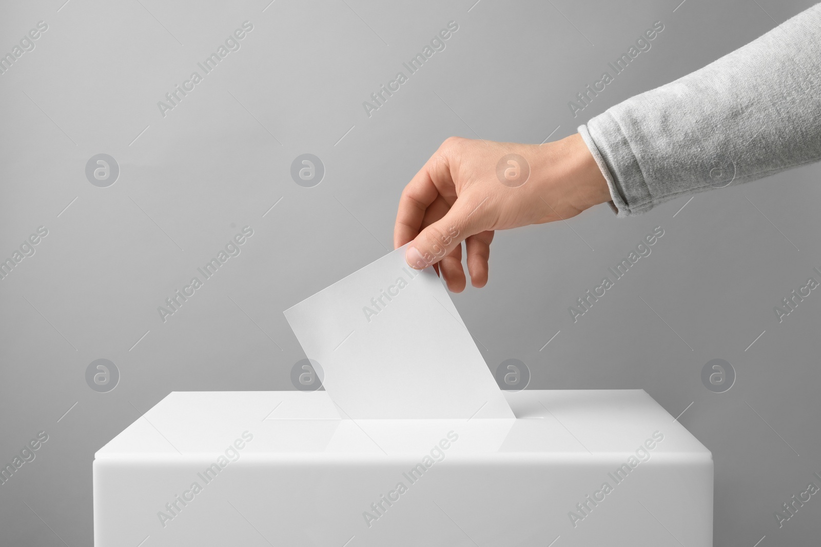 Photo of Man putting his vote into ballot box on light background, closeup