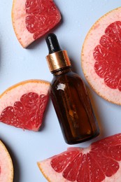 Photo of Bottle of cosmetic serum and grapefruit slices on light blue background, flat lay