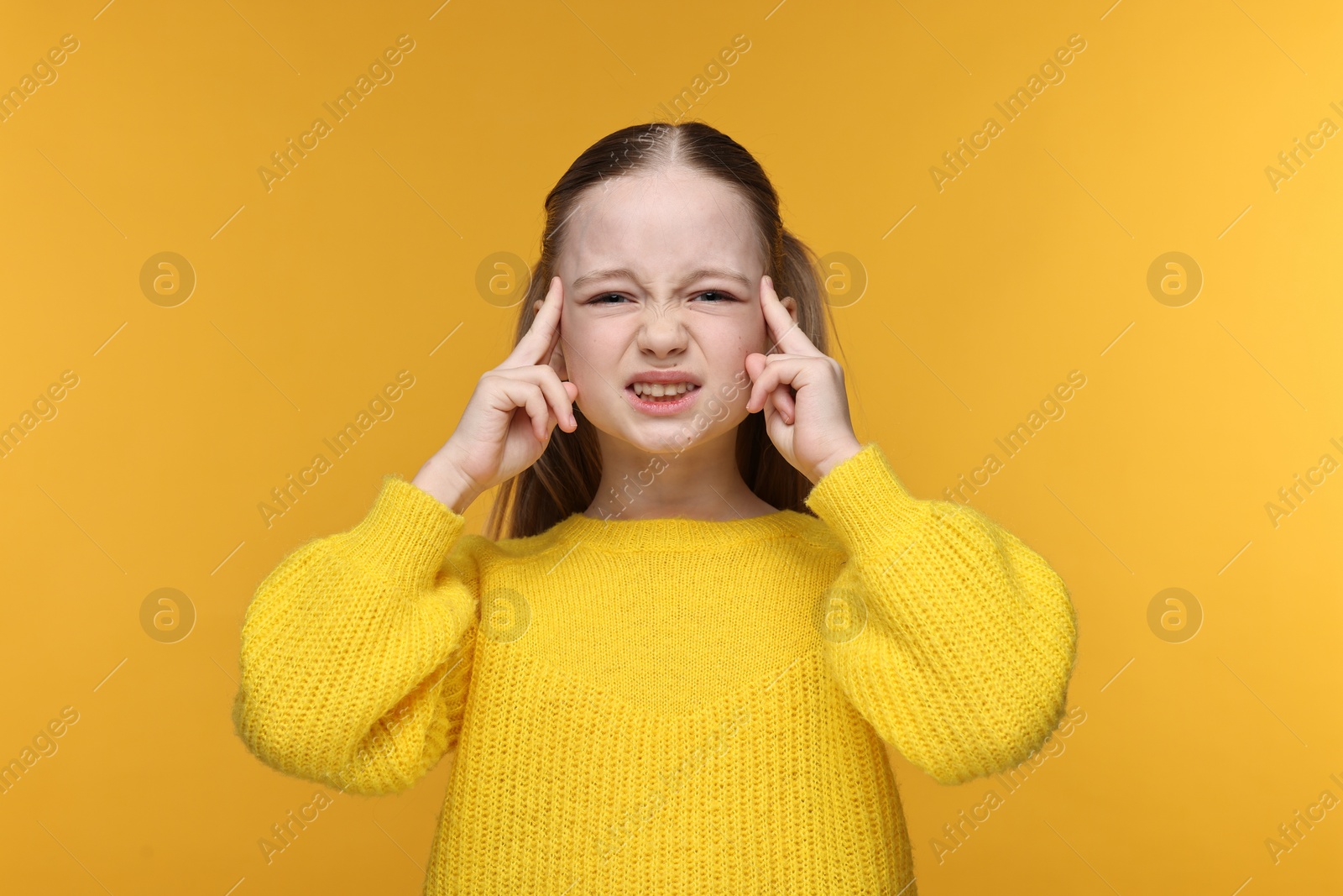 Photo of Little girl suffering from headache on yellow background