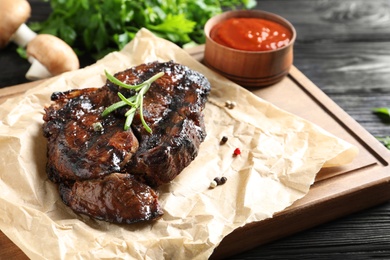 Photo of Delicious barbecued steak served with sauce on wooden board