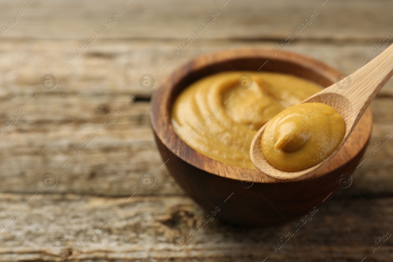 Photo of Spoon and bowl with tasty mustard sauce on wooden table, closeup. Space for text