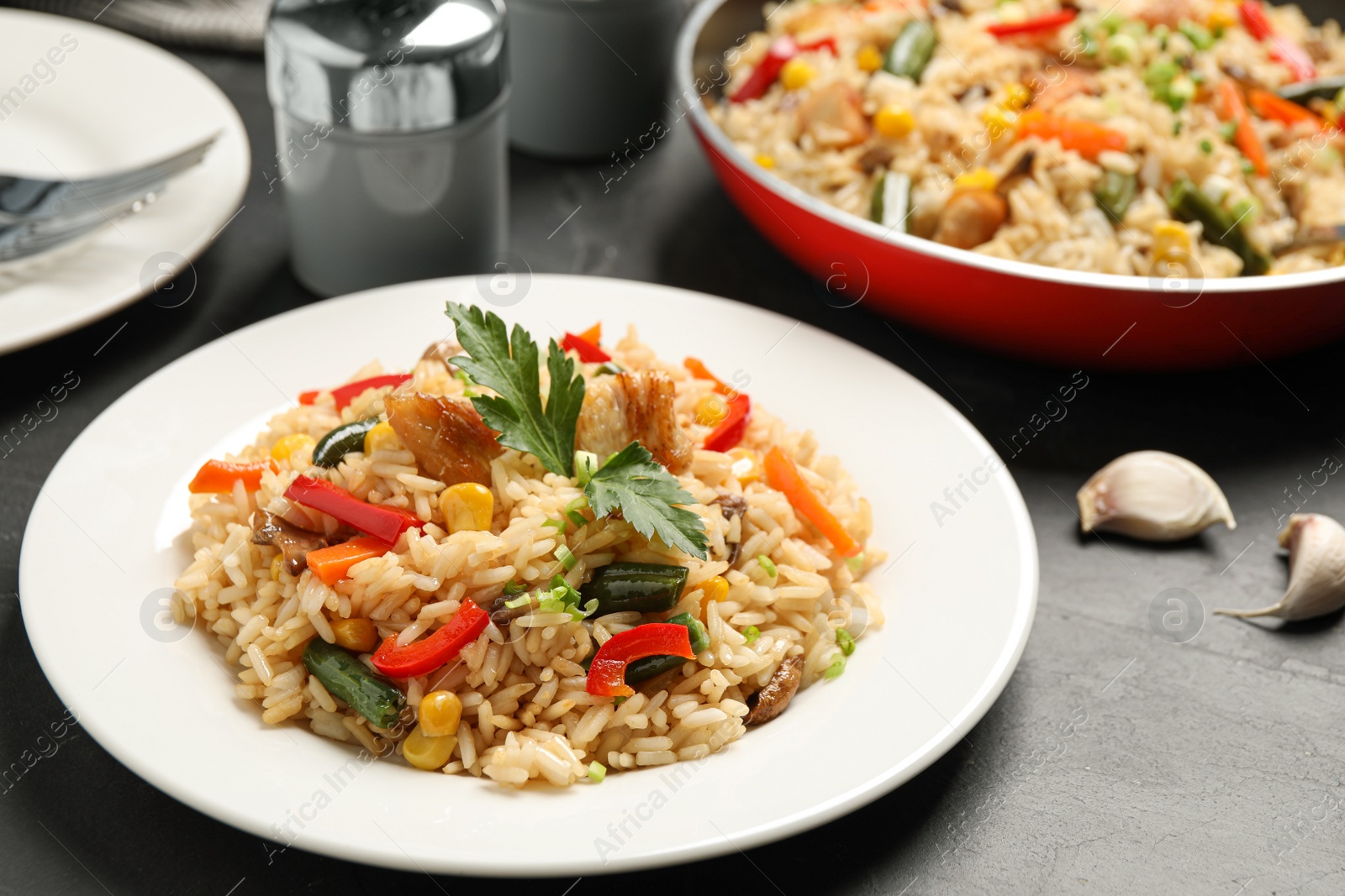 Photo of Delicious rice pilaf with chicken and vegetables on black table