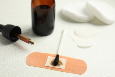 Photo of Cotton bud with medical iodine and sticking plaster on white wooden table, closeup