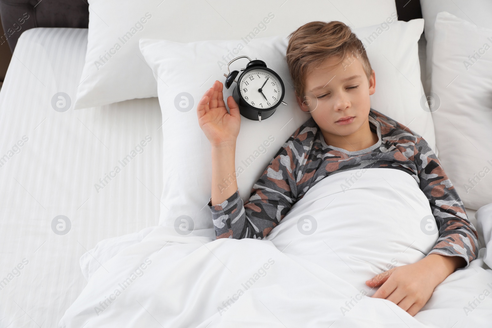 Photo of Cute boy with alarm clock sleeping in bed, above view. Space for text