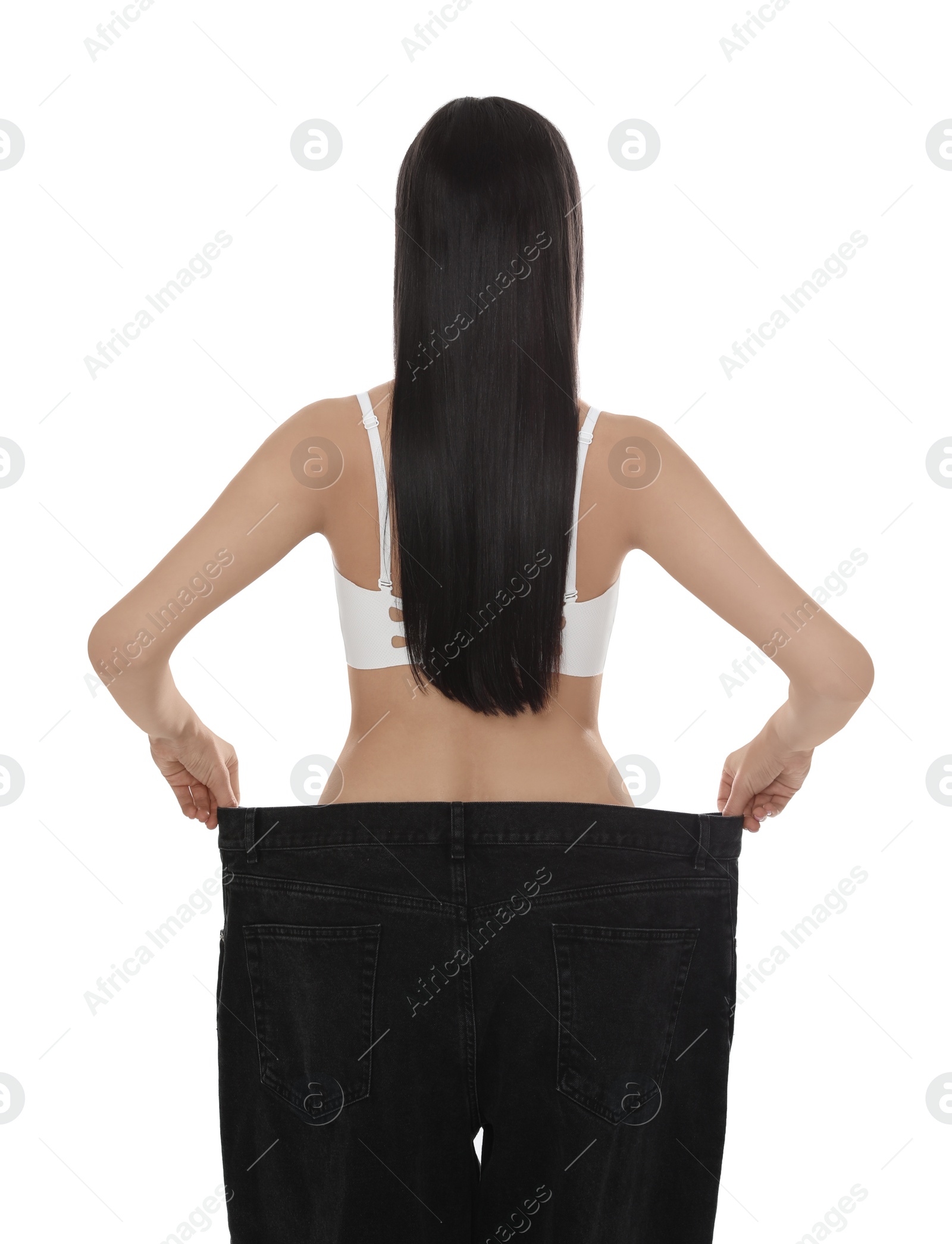 Photo of Young woman wearing big jeans after weight loss on white background, back view