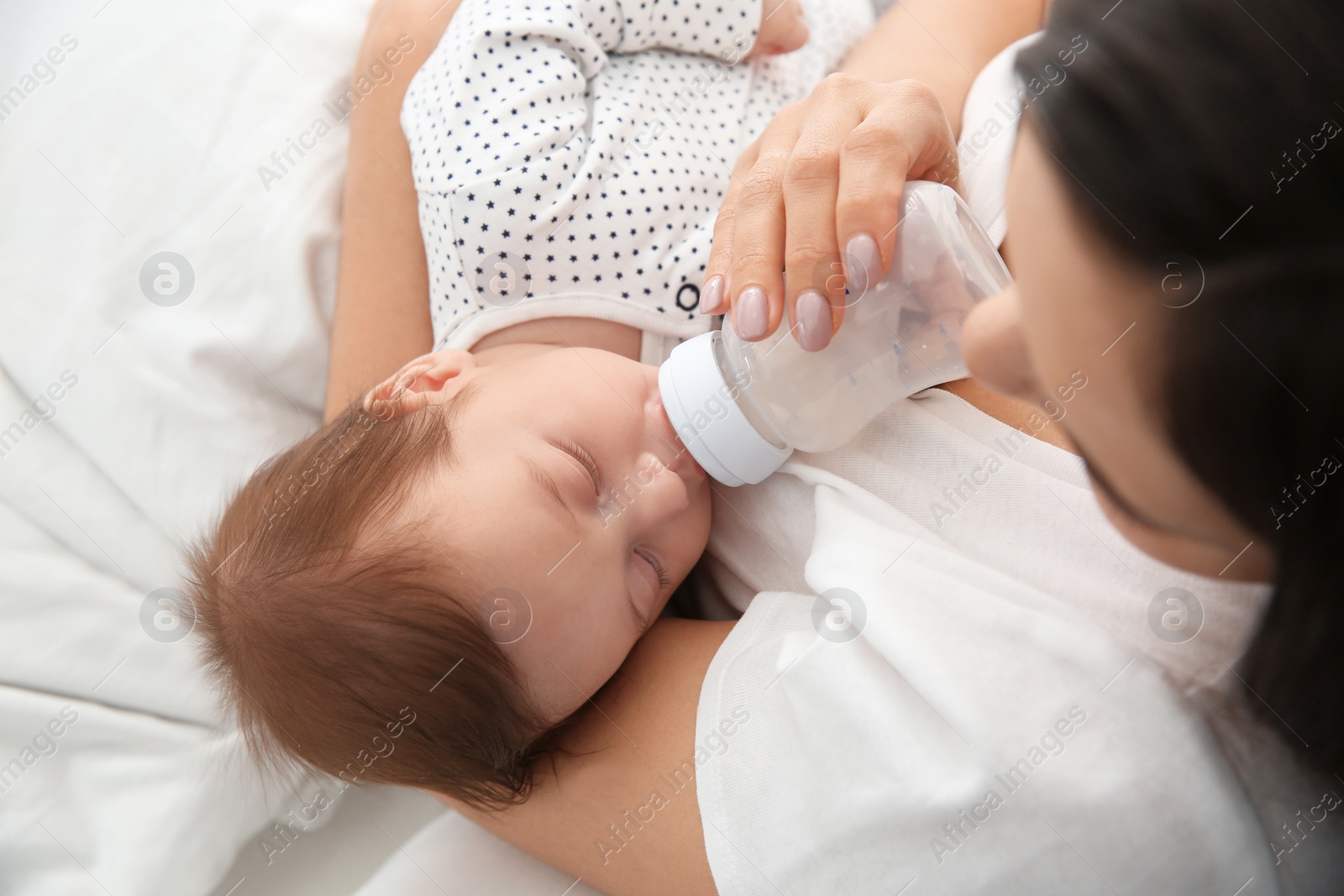 Photo of Woman feeding her baby from bottle on bed, closeup