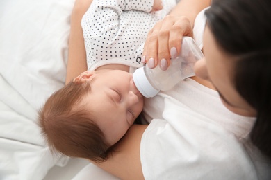 Woman feeding her baby from bottle on bed, closeup